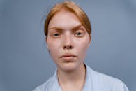 Close-up studio portrait of a serious, freckled woman with red hair and blue eyes against a plain background.